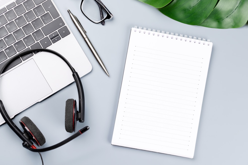 Headset, Laptop und Notizblock auf einem Schreibtisch